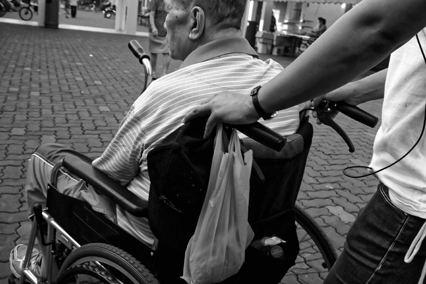 young man pushing an elderly man in a wheelchair